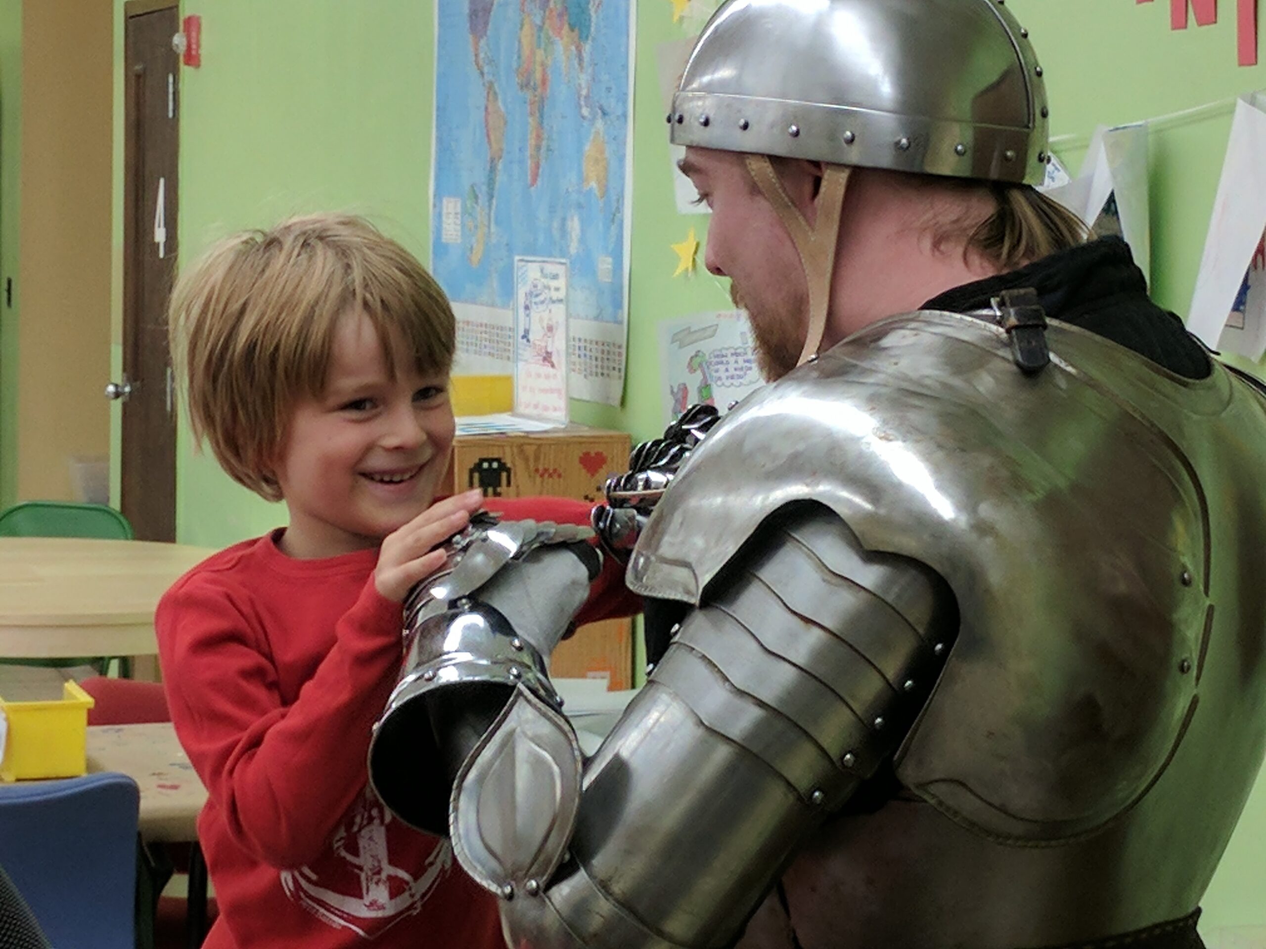 Image shows a teacher in historical plate armor holding his hand out to a child.