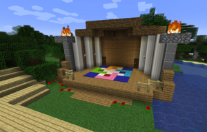 Screenshot of a Minecraft building: A covered stage made of wood, with the Einstein's Workshop Logo in wool on the stage. Auditorium-style seating made of wooden stairs in the foreground.